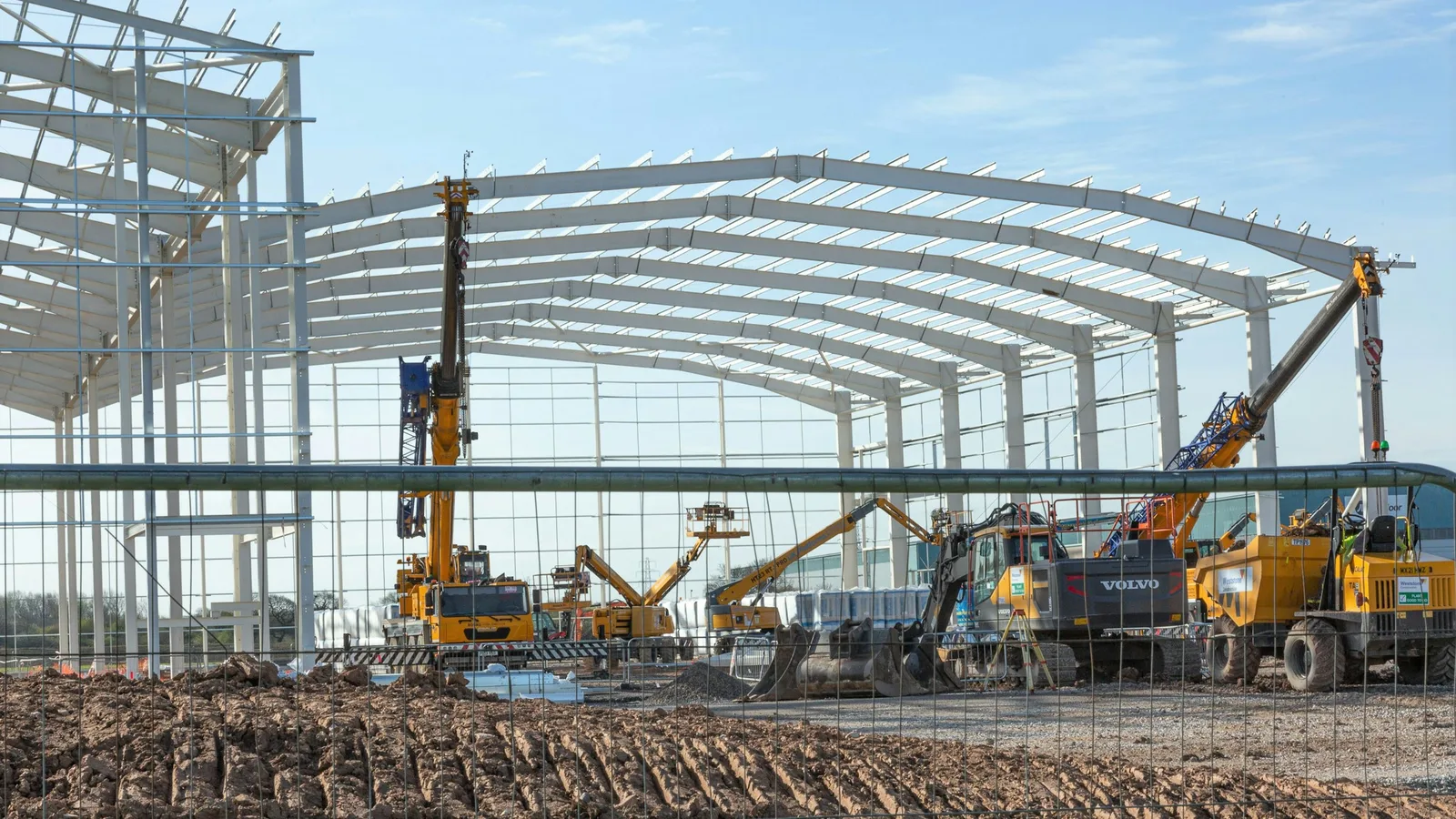 Modern industrial warehouse under construction with steel frame and cranes, industrial real estate lawyer in Guadalajara